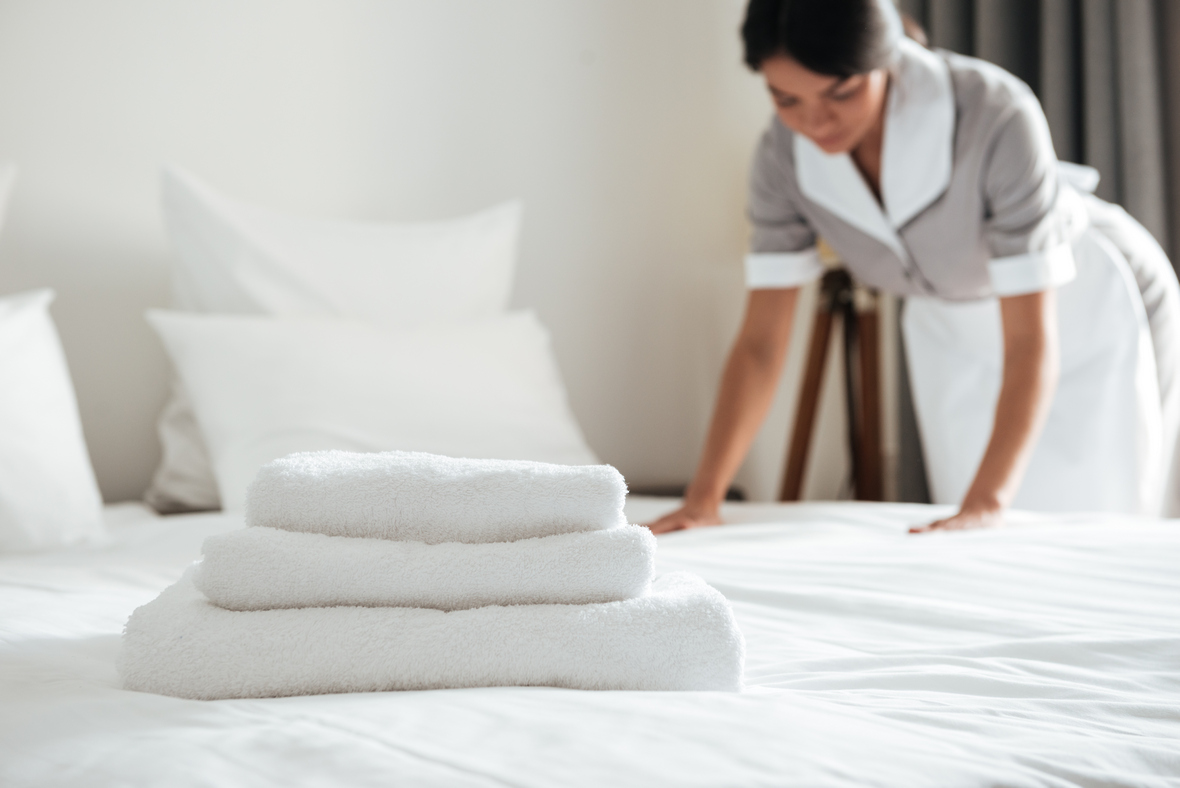 Young hotel maid making the bed with clean fresh towels